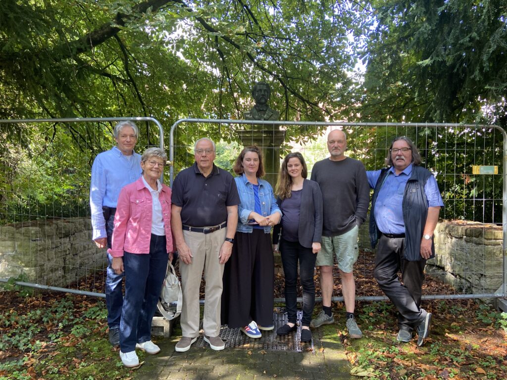 Vertreterinnen und Vertreter des Verschönerungsvereins, der Stadtverwaltung und der ausführenden Firma am 15. Juli 2025 vor dem Bauzaun im Zanders-Büstengarten. Von links nach rechts: Dr. Albert Eßer, Geschäftsführer des Verschönerungsvereins; Helga Monheim, stellvertretende Vorsitzende des Verschönerungsvereins; Franz Josef Vierkotten, Vorsitzender des Verschönerungsvereins; Frau A. Peters, Vertreterin der Unteren Denkmalbehörde Bergisch Gladbach; Anna Bandke, Vertreterin der Stadtverwaltung Bergisch Gladbach; Herr Hajo Blenk, Vertreter der mit den Arbeiten beauftragten Firma Schwieren; Prof. Dr. Michael Werling, stellvertretender Vorsitzender des Verschönerungsvereins Foto: Christian Ruhe