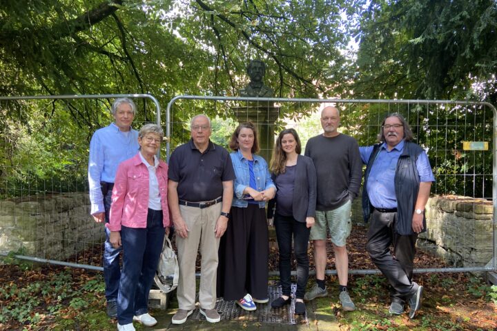 Vertreterinnen und Vertreter des Verschönerungsvereins, der Stadtverwaltung und der ausführenden Firma am 15. Juli 2025 vor dem Bauzaun im Zanders-Büstengarten. Von links nach rechts: Dr. Albert Eßer, Geschäftsführer des Verschönerungsvereins; Helga Monheim, stellvertretende Vorsitzende des Verschönerungsvereins; Franz Josef Vierkotten, Vorsitzender des Verschönerungsvereins; Frau A. Peters, Vertreterin der Unteren Denkmalbehörde Bergisch Gladbach; Anna Bandke, Vertreterin der Stadtverwaltung Bergisch Gladbach; Herr Hajo Blenk, Vertreter der mit den Arbeiten beauftragten Firma Schwieren; Prof. Dr. Michael Werling, stellvertretender Vorsitzender des Verschönerungsvereins Foto: Christian Ruhe